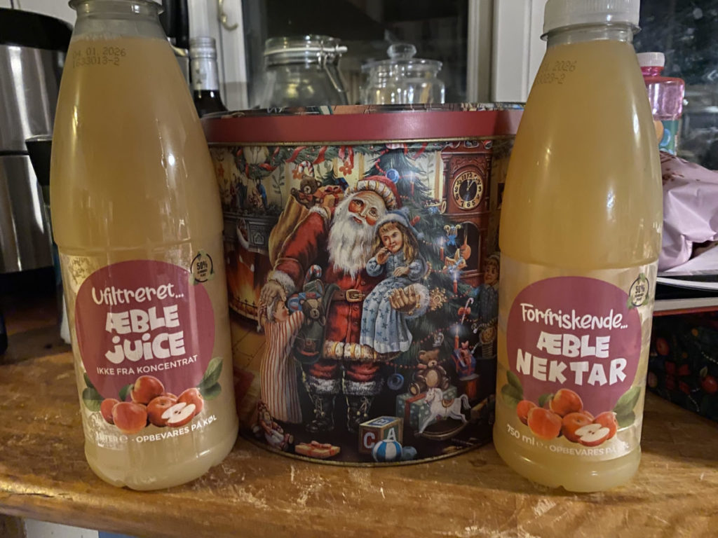 Johannes' drikkevarer står på hver sin side af ne dejligt glansbilledeagtig kagedåse med en julemand på.